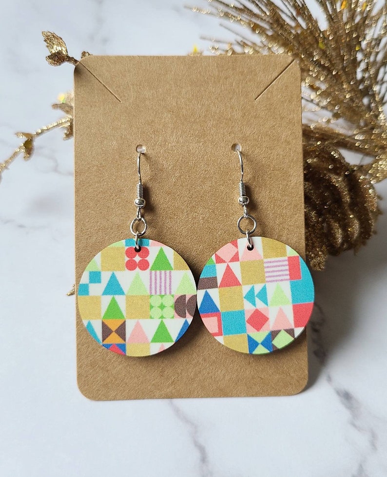 May include: A pair of colourful geometric pattern earrings. The earrings are round and made of wood with silver hooks.