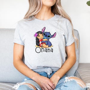 May include: A gray t-shirt with a cartoon image of Stitch hugging Lilo. The shirt has the word "Ohana" printed below the image.