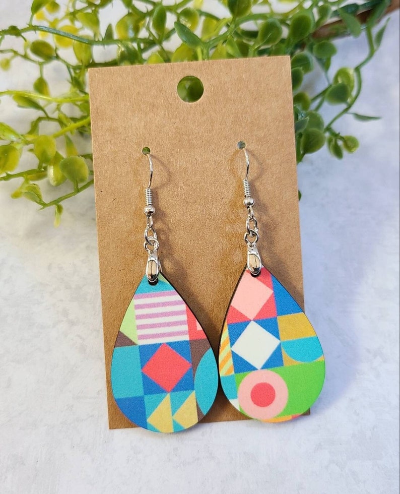 May include: A pair of teardrop-shaped earrings with a geometric pattern in shades of blue, green, pink, yellow, and white. The earrings are made of wood and have silver hooks.