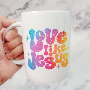 May include: White ceramic coffee mug with a rainbow-colored design that says "Love like Jesus" with gold glitter accents.