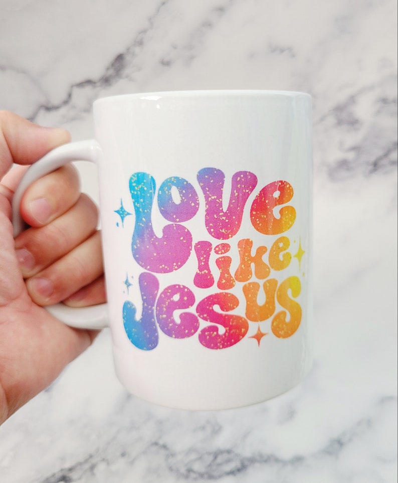 May include: White ceramic coffee mug with a rainbow-colored design that says "Love like Jesus" with gold glitter accents.