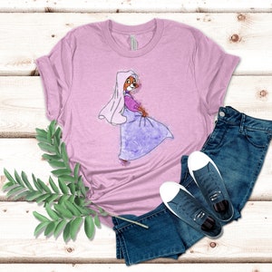 Op de afbeelding: Een roze T-shirt met een aquarel-illustratie van een cartoonvos die een paarse jurk en een witte sluier draagt. De vos kijkt naar rechts en heeft een roze neus en bruine ogen.