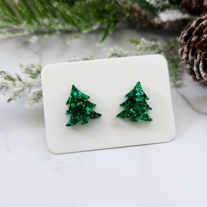 May include: A pair of green glitter Christmas tree earrings. The earrings are small and have a simple design.