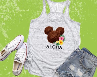 May include: A white tank top with a brown coconut Mickey Mouse design and the word "Aloha" printed on the front. The tank top is paired with denim shorts.