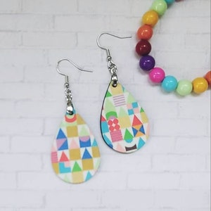 May include: A pair of teardrop-shaped earrings with a colourful geometric pattern. The earrings are made of wood and have silver hooks.