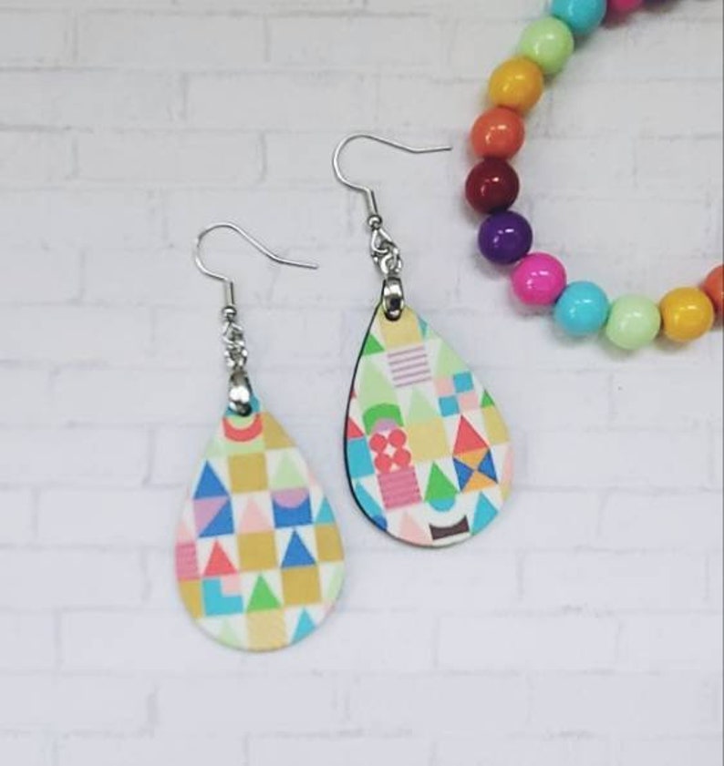 May include: A pair of teardrop-shaped earrings with a colourful geometric pattern. The earrings are made of wood and have silver hooks.