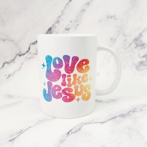 May include: White ceramic coffee mug with a rainbow-colored design that says "Love like Jesus" in a retro font.