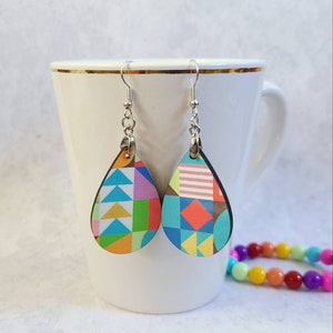 May include: A pair of teardrop-shaped earrings with a colourful geometric pattern. The earrings are made of wood and have silver hooks.