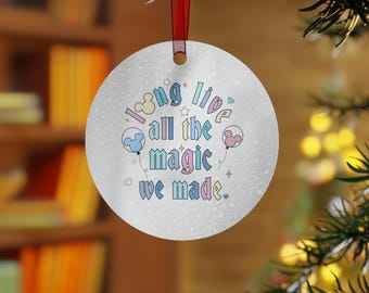 以下が含まれることがあります： 「Long live all the magic we made」の文字が入った丸い銀色のクリスマスオーナメント。パステルカラーでミッキーマウスの頭の風船が描かれています。吊り下げ用の赤いリボンが付いています。オーナメントはクリスマスツリーに飾られています。