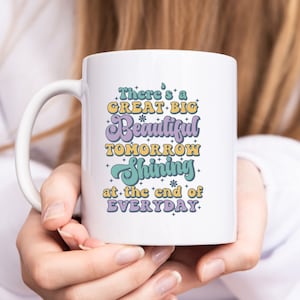 May include: White ceramic mug with a colorful graphic that reads "There's a GREAT BIG Beautiful TOMORROW Shining at the end of EVERYDAY."