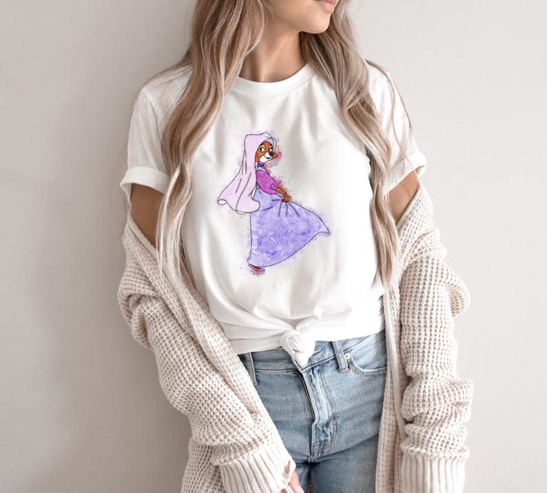 Op de afbeelding: Wit T-shirt met een cartoonillustratie van een vos die een paarse jurk en een roze sluier draagt. De vos kijkt naar rechts en heeft een roze blos op zijn wangen.