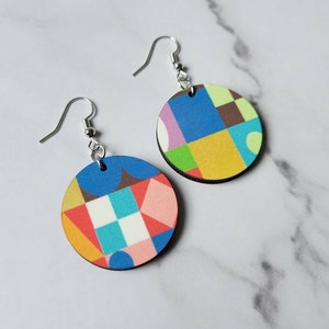 May include: A pair of colourful geometric pattern earrings. The earrings are round and made of wood. The pattern is a mix of blue, green, yellow, red, and white.