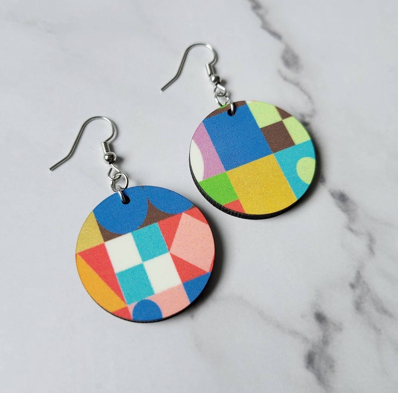 May include: A pair of colourful geometric pattern earrings. The earrings are round and made of wood. The pattern is a mix of blue, green, yellow, red, and white.