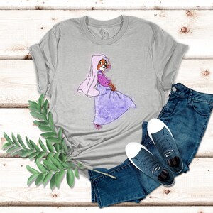 Op de afbeelding: Een heidekleurig t-shirt met een aquarel-illustratie van een cartoonvos die een paarse jurk en een roze sluier draagt.