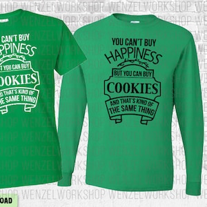 May include: Two green t-shirts with the text "You can't buy happiness but you can buy cookies and that's kind of the same thing" printed on them. One t-shirt has white text and the other has black text.