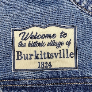 May include: A blue denim jacket with a white patch that says "Welcome to the historic village of Burkittsville 1824".