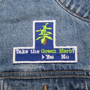 Op de afbeelding: Blauw en wit geborduurde patch met een groene plant en de tekst "Take the Green Herb? Yes No".