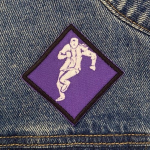 May include: Purple diamond-shaped patch with a white outline. The patch features a white silhouette of a person dancing.
