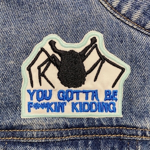 May include: A blue denim jacket with a black and white embroidered patch that says "You gotta be f***in' kidding".