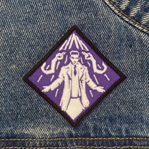 May include: Purple diamond-shaped patch with white embroidered design of a person with arms outstretched, surrounded by white lines. The person is wearing a white coat and has a white face with black eyes.