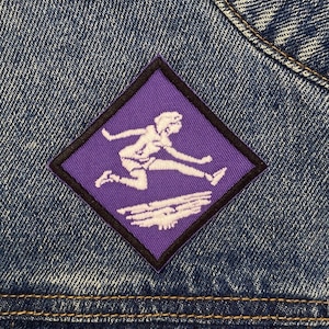 May include: Purple diamond-shaped patch with a white outline. The patch features a white silhouette of a person jumping over a white wave.