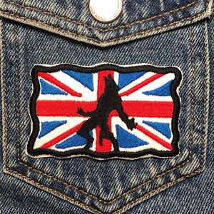 Könnte beinhalten: Eine blaue Jeansjacke mit einem Patch auf der Tasche. Der Patch ist eine schwarze Silhouette einer Person, die auf einer Union Jack-Flagge steht.