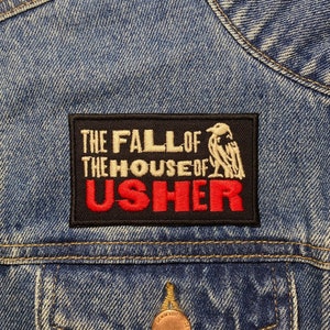 May include: A black and red embroidered patch with the text "The Fall of the House of Usher" on a denim jacket.