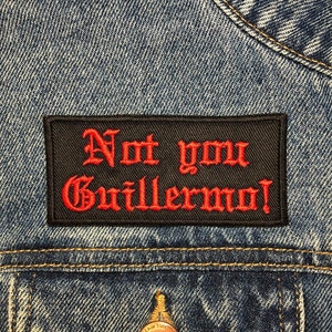 以下が含まれることがあります： 青いデニムジャケットに、「Not you Guillermo!」という赤い刺繍の文字が書かれた黒いパッチ