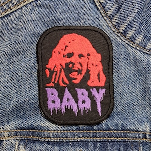 May include: A black patch with a red and purple design of a screaming face and the word "BABY" in purple dripping letters. The patch is sewn onto a blue denim jacket.