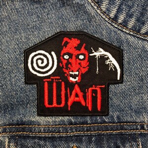 May include: A black and red embroidered patch with a spiral, a red demon face, and a white stick figure hanging from a rope. The text "WAN" is embroidered in red on a black background.