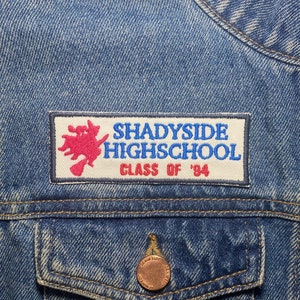 Op de afbeelding: Een blauwe denimjas met een witte patch waarop staat "Shadyside Highschool Class of '94". De patch heeft een rode en witte illustratie van een draak.