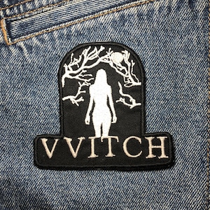 May include: A black patch with a white silhouette of a woman under a tree design. The patch has the word "VVITCH" in white letters at the bottom. The patch is sewn onto a blue denim jacket.