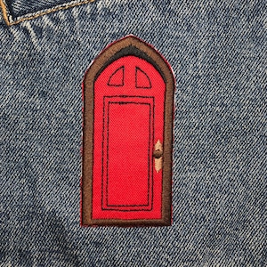 Könnte beinhalten: Roter Tür-Stickerei-Aufnäher auf blauem Jeansstoff. Die Tür hat einen braunen Rahmen und ein kleines Fenster mit zwei Scheiben.