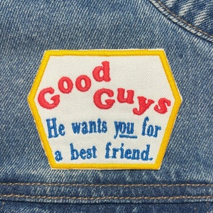 Könnte beinhalten: Ein weißer Patch mit gelber Naht, der auf eine blaue Jeansjacke genäht ist. Der Patch hat die Form eines Sechsecks und trägt den Text "Good Guys" in roten und weißen Buchstaben. Unter dem Text steht der Satz "He wants you for a best friend."