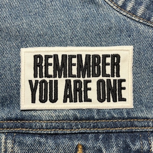 Könnte beinhalten: Eine blaue Jeansjacke mit einem weißen Patch, auf dem in schwarzer Schrift "Remember You Are One" steht.