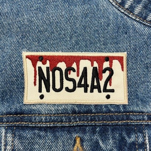 May include: A denim jacket with a red and white patch that says "NOS4A2" in black lettering. The patch has red dripping paint on the top.
