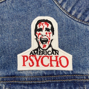 Peut inclure: Un patch brodé blanc et rouge avec un contour noir. Le patch représente un dessin animé d'un homme avec du sang sur le visage et le texte "AMERICAN PSYCHO".