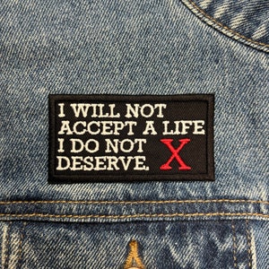 May include: Black and white embroidered patch with the text "I will not accept a life I do not deserve." A red "X" is embroidered in the center of the patch.