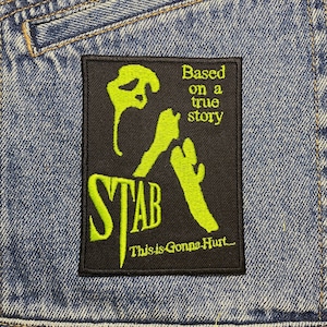 Peut inclure: Patch brodé noir et vert avec une silhouette d'une personne tenant un couteau. Le texte "STAB" est en vert et les textes "Based on a true story" et "This is Gonna Hurt..." sont en blanc.