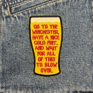 Può includere: Giacca di jeans blu con una toppa gialla a forma di bicchiere di birra. La toppa presenta il testo rosso: "GO TO THE WINCHESTER, HAVE A NICE COLD PINT, AND WAIT FOR ALL OF THIS TO BLOW OVER".