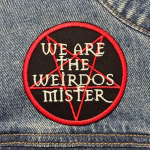 May include: A round black patch with a red border and a red pentagram design. The patch has the white text "WE ARE THE WEIRDOS MISTER". The patch is sewn onto a blue denim jacket.