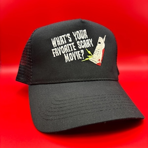 May include: Black trucker hat featuring the text "WHAT'S YOUR FAVORITE SCARY MOVIE?" in white, and an embroidered graphic of a phone with red and white details. The hat has a black brim and a mesh back.