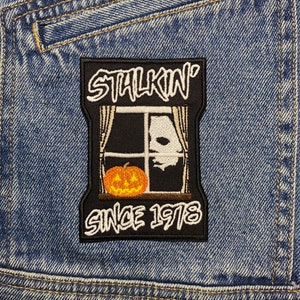 Può includere: Toppa ricamata in bianco e nero con il testo "Stalkin' Since 1978" e un'immagine di una finestra con una zucca e un fantasma all'interno.
