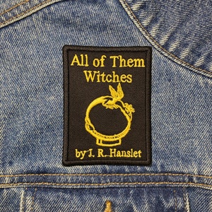 May include: A black and gold embroidered patch with the text "All of Them Witches" and "by J. R. Hanslet".
