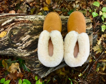 Puede incluir: Un par de zapatillas de color marrón claro con forro de borrego crema. Las zapatillas están hechas de material suave y están diseñadas para uso en interiores. La imagen es desde arriba, mostrando el diseño acogedor.