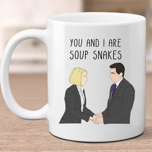 May include: White ceramic mug featuring the text "YOU AND I ARE SOUP SNAKES" and an illustration of two people shaking hands. The figures are dressed in business attire.