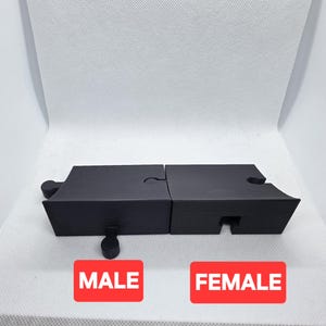 Pode incluir: Pe&ccedil;as de quebra-cabe&ccedil;a pretas com um design masculino e feminino. As pe&ccedil;as est&atilde;o conectadas, e a palavra "MALE" &eacute; impressa em um ret&acirc;ngulo vermelho, e a palavra "FEMALE" &eacute; impressa em outro ret&acirc;ngulo vermelho.