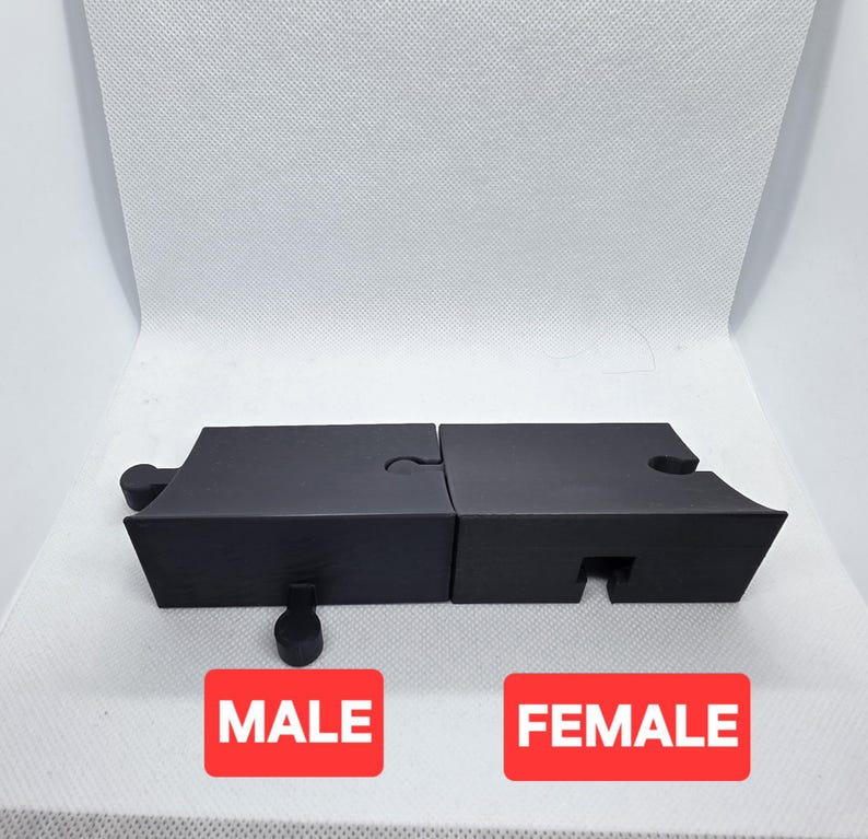 Pode incluir: Pe&ccedil;as de quebra-cabe&ccedil;a pretas com um design masculino e feminino. As pe&ccedil;as est&atilde;o conectadas, e a palavra "MALE" &eacute; impressa em um ret&acirc;ngulo vermelho, e a palavra "FEMALE" &eacute; impressa em outro ret&acirc;ngulo vermelho.