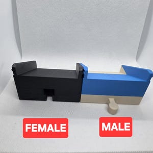 Pode incluir: Um objeto impresso em 3D de duas partes e multicolorido. Uma se&ccedil;&atilde;o &eacute; preta, a outra &eacute; azul e bege. A palavra "FEMALE" &eacute; impressa em um ret&acirc;ngulo vermelho, e "MALE" em outro ret&acirc;ngulo vermelho.
