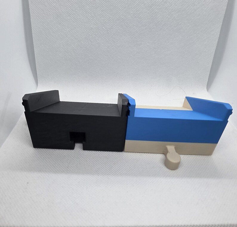 Pode incluir: Um brinquedo de madeira geom&eacute;trico multicolorido. O brinquedo &eacute; principalmente preto e azul, com uma base bege. Tem uma forma retangular com um pequeno pino bege saliente. O brinquedo &eacute; projetado com uma ranhura e uma se&ccedil;&atilde;o elevada.